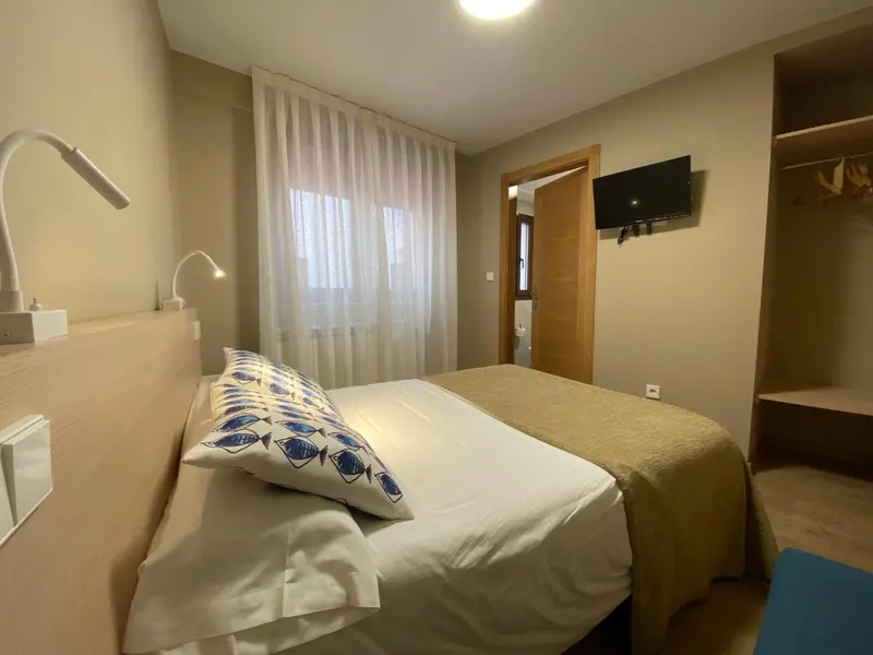 Une chambre lumineuse avec un lit double et une télévision murale.