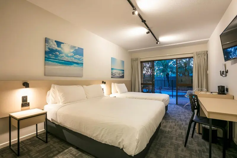 Une chambre lumineuse avec un grand lit et un bureau près d'une baie vitrée.