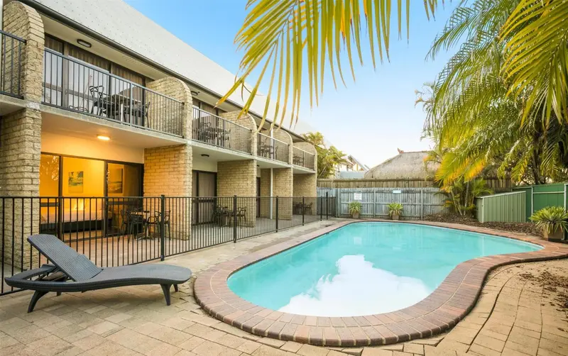 Une piscine turquoise est entourée d'une terrasse avec des transats et des palmiers.