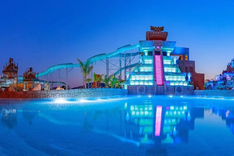 Structure aquatique illuminée avec toboggans et bassins reflétés dans l'eau.