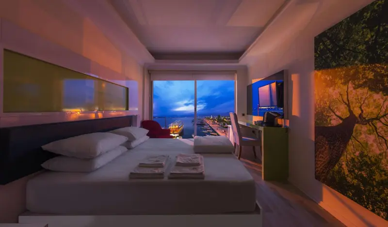 Chambre moderne avec un grand lit et une vue sur la mer au crépuscule.