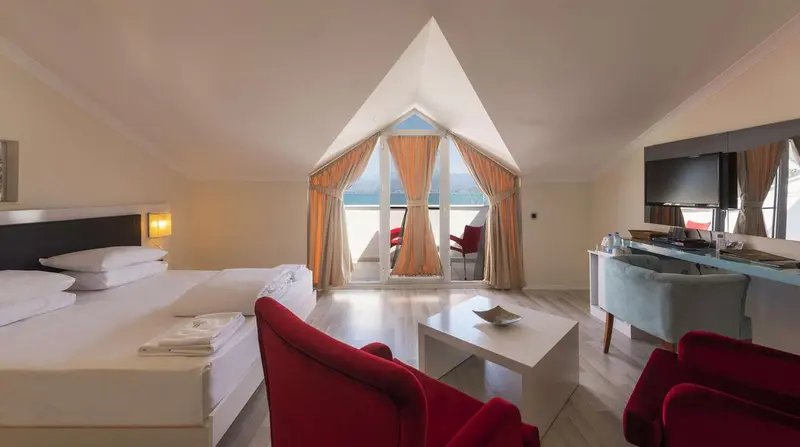 Chambre lumineuse avec lit double, coin salon et vue sur la mer.