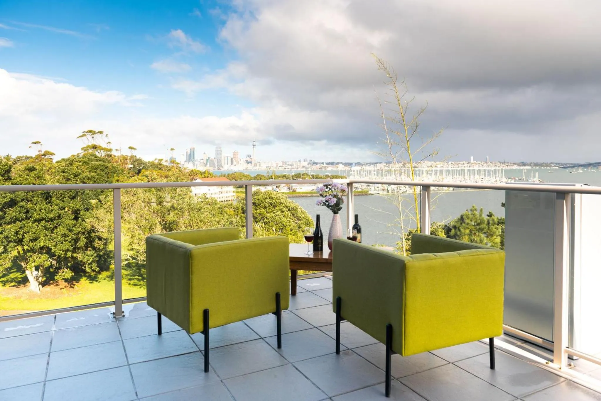 Terrasse avec deux fauteuils verts et vue sur la ville et la mer.