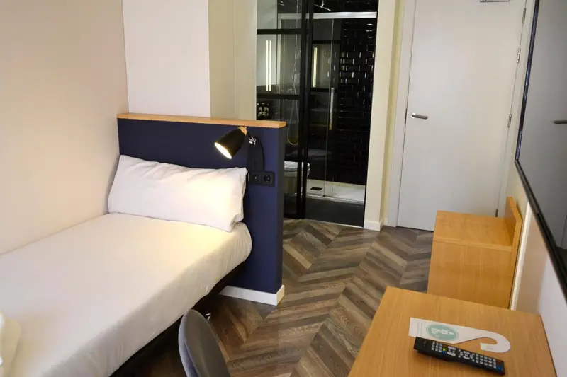 Une chambre moderne avec un lit simple et une salle de bain vitrée.