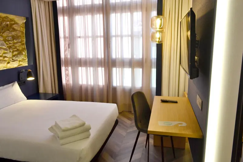 Une chambre lumineuse avec un lit, un bureau et des rideaux.