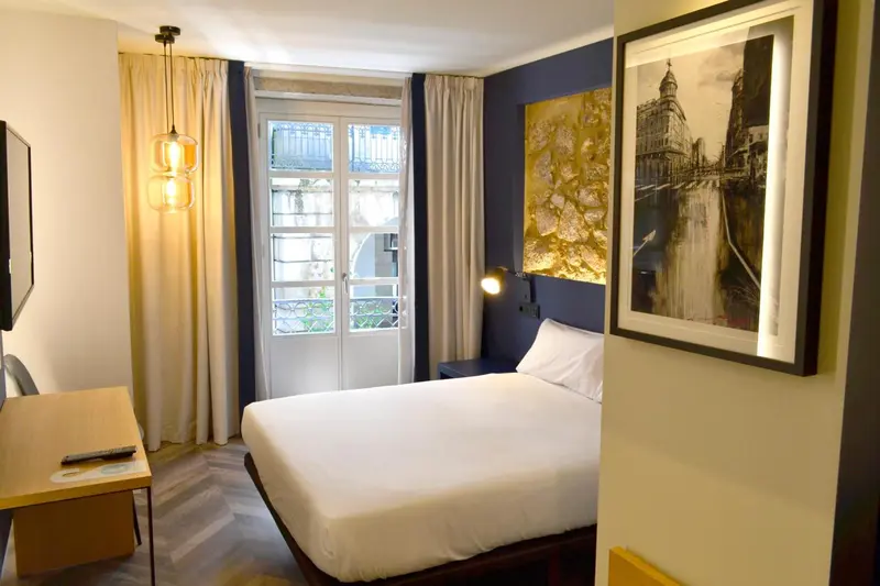 Une chambre lumineuse avec un lit double et un accès à un balcon.