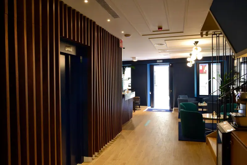 Un couloir mène à une réception et un espace salon avec des canapés verts.