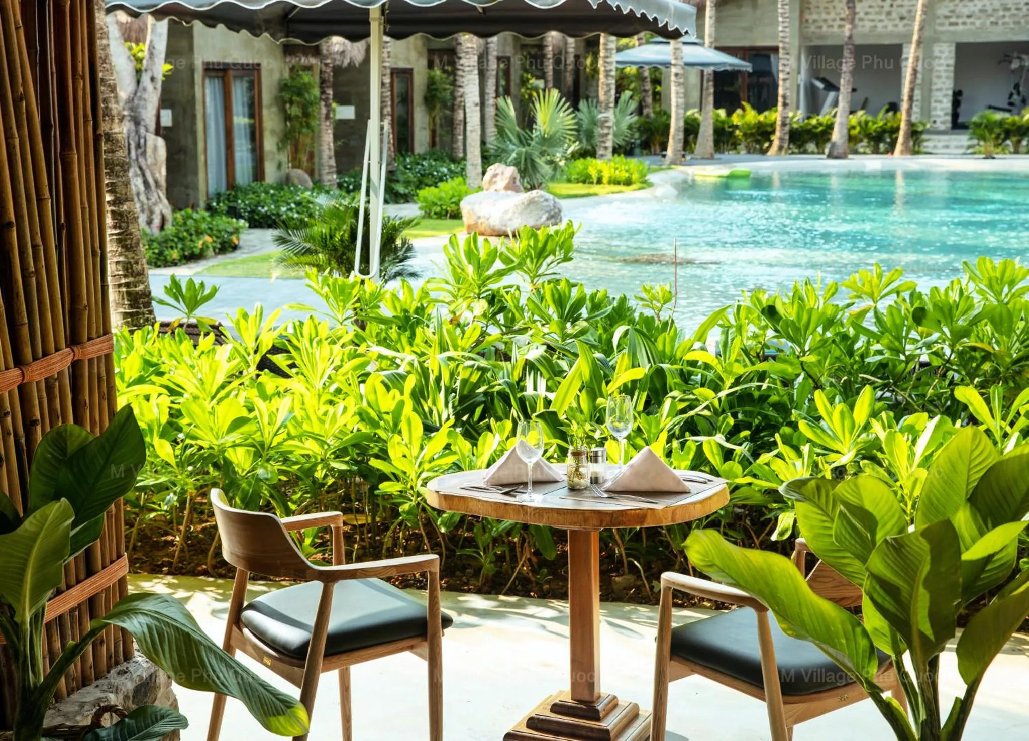 Une table est dressée devant une piscine bordée de végétation tropicale.