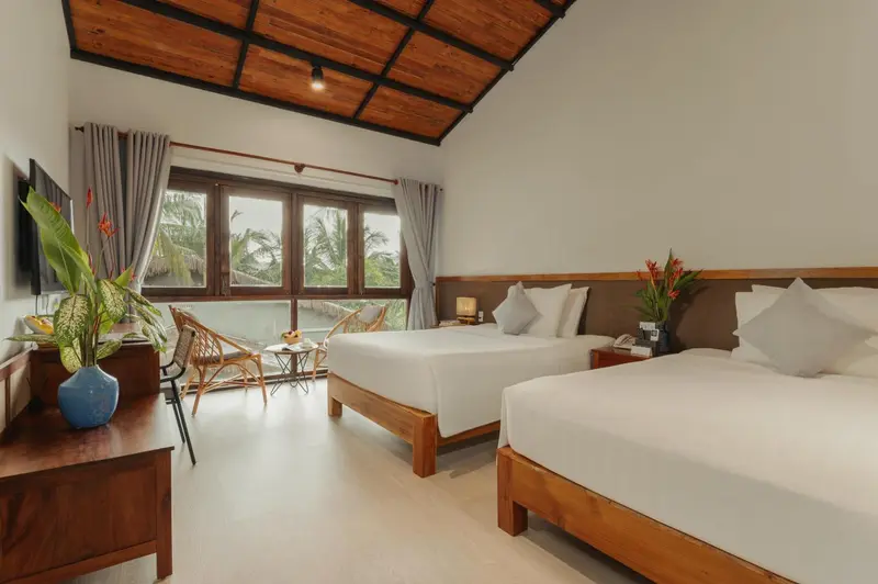 Chambre lumineuse avec deux lits simples et vue sur la végétation.