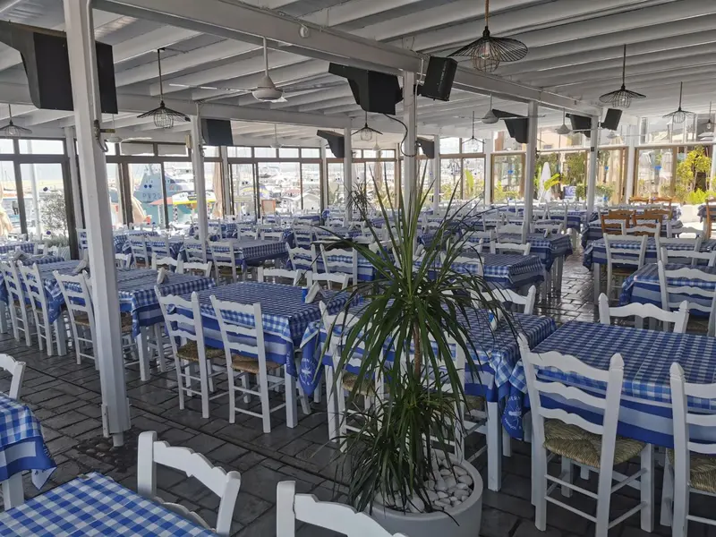 Une salle de restaurant lumineuse avec des tables dressées et une vue sur un port.
