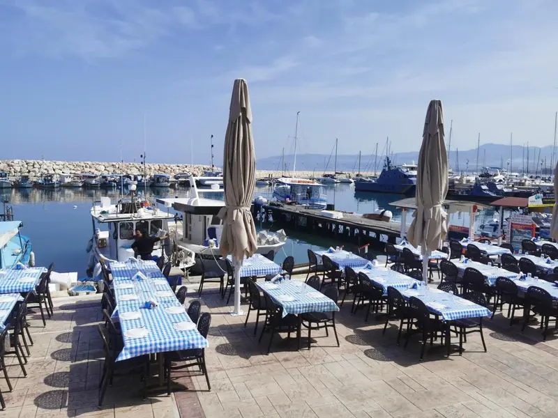 Tables dressées en terrasse avec vue sur un port de plaisance ensoleillé.
