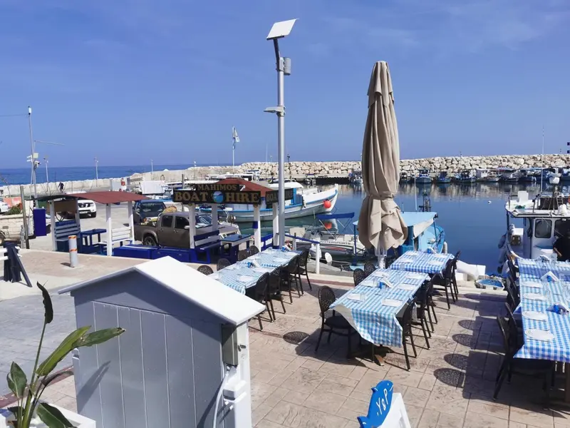 Terrasse ombragée avec tables et chaises donnant sur un port de plaisance.