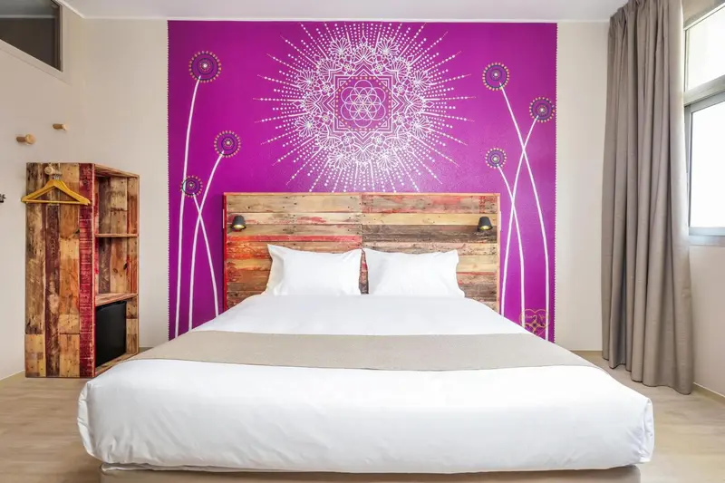 Une chambre avec un grand lit recouvert d'une couette blanche et d'un couvre-lit gris.