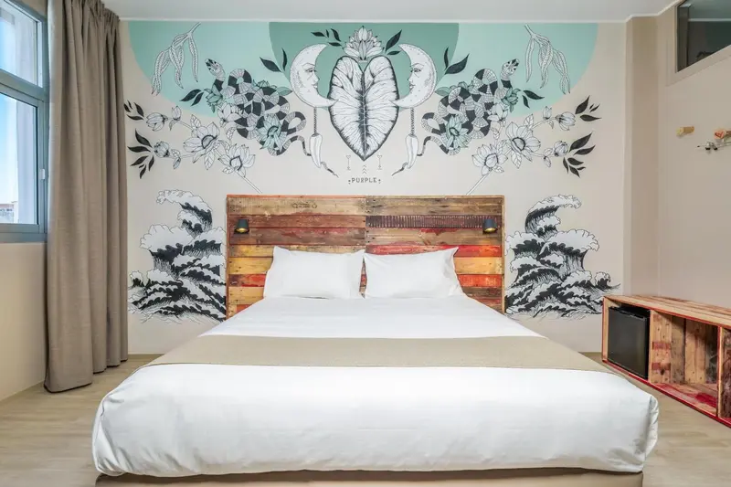 Une chambre lumineuse avec un grand lit et un mur décoré d'une fresque florale.
