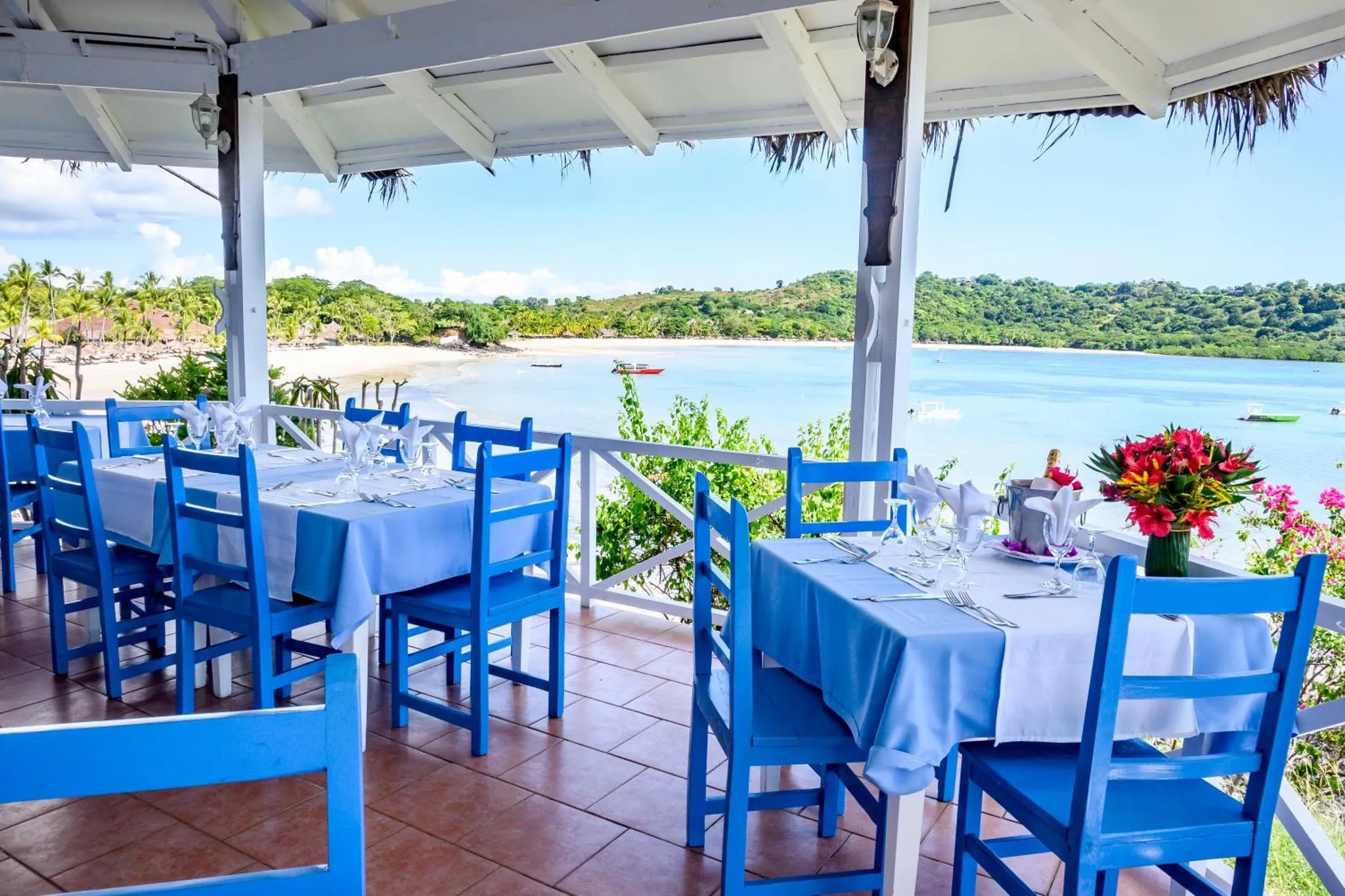 Une terrasse ombragée avec des tables dressées face à la mer.