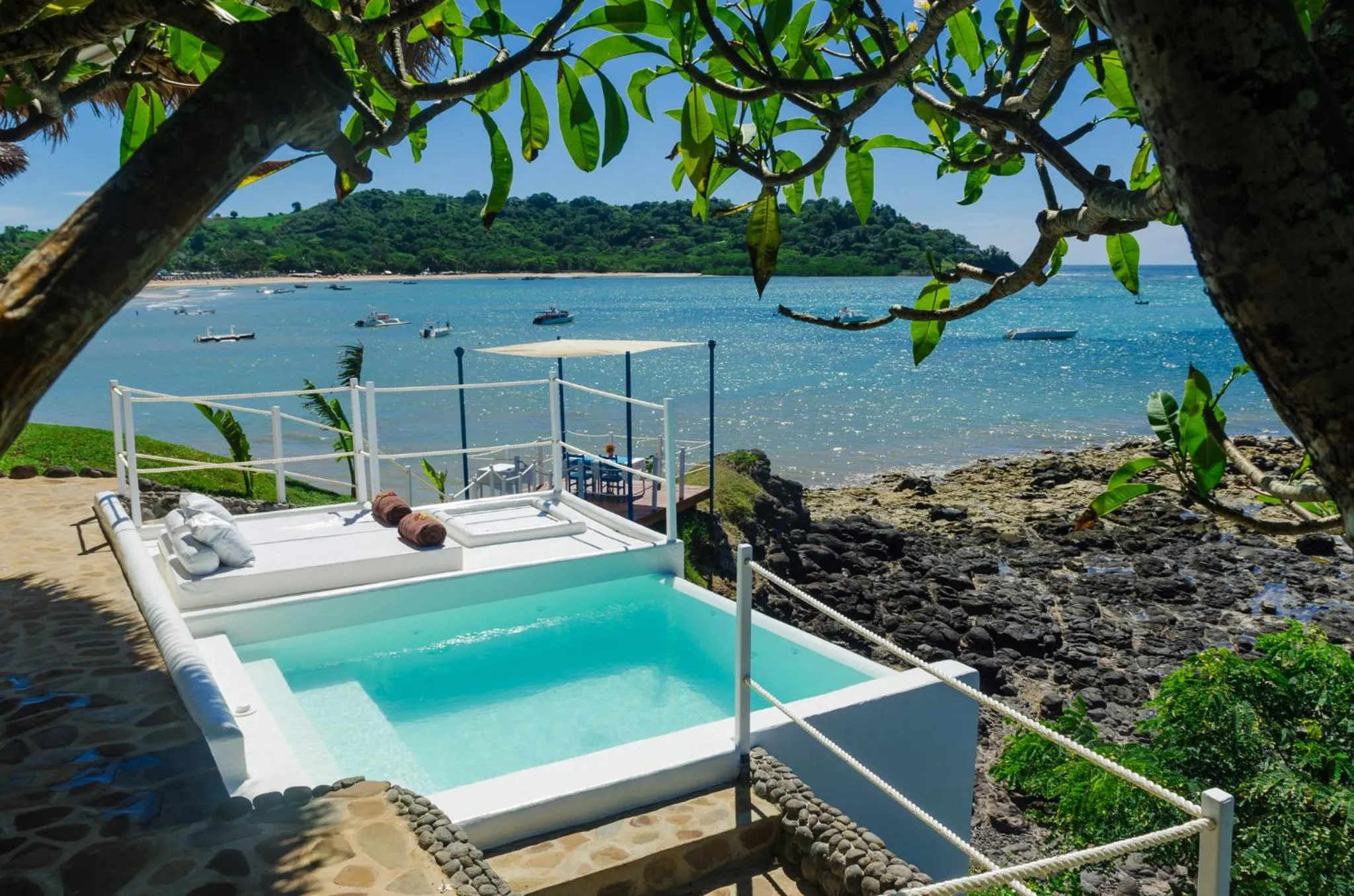 Petite piscine rectangulaire avec transats sur une terrasse ensoleillée face à la mer.
