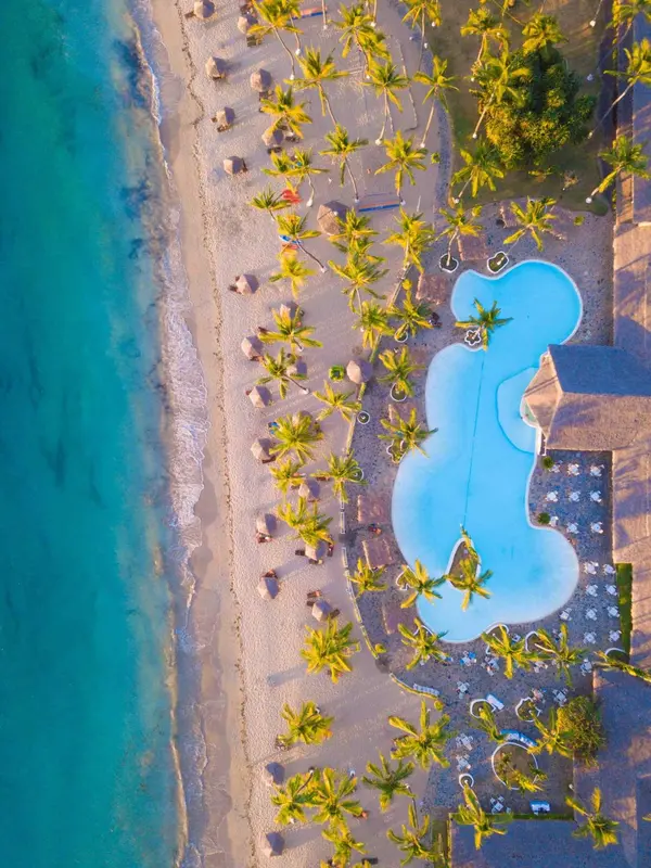 Vue aérienne d'une plage bordée de palmiers et d'une piscine turquoise.