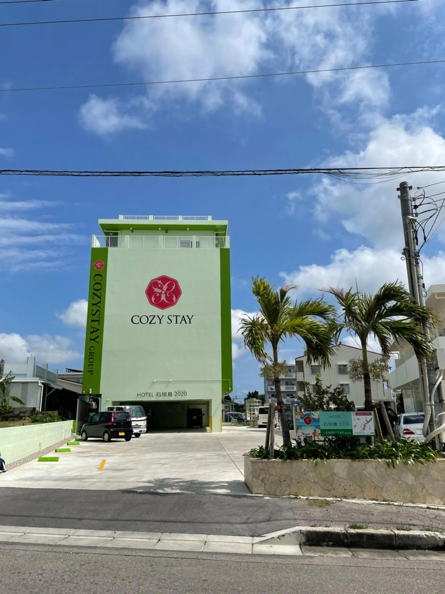 Bâtiment vert à plusieurs étages avec une entrée et des palmiers.