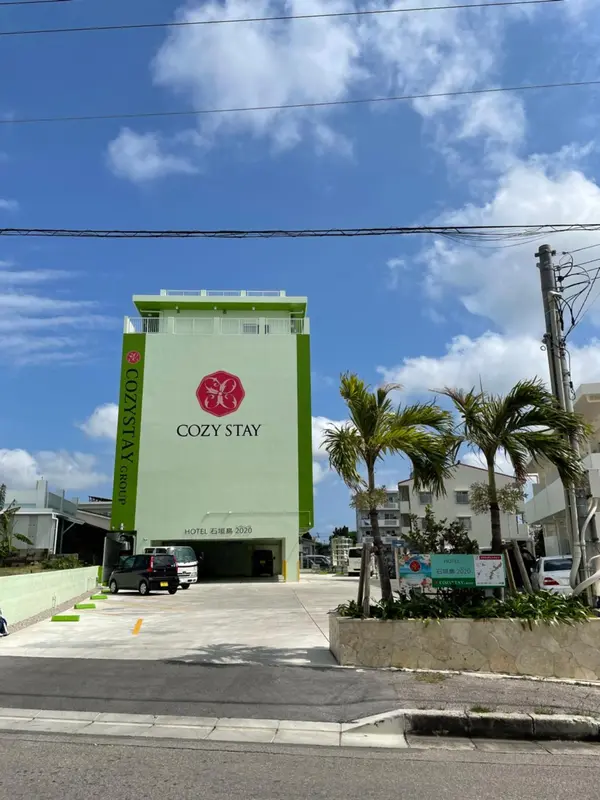 Bâtiment vert à plusieurs étages avec une entrée et des palmiers.