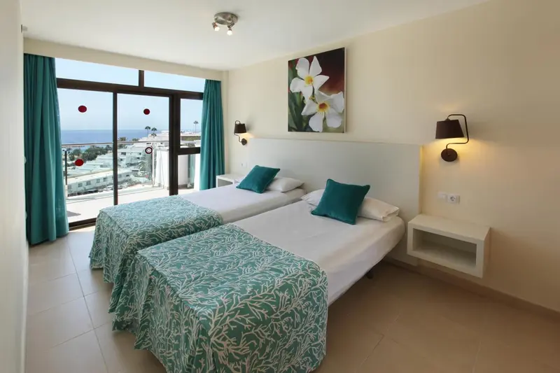 Chambre lumineuse avec deux lits simples donnant sur une vue mer.
