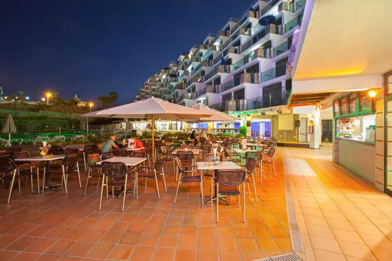Terrasse lumineuse avec tables et chaises devant un bâtiment éclairé.