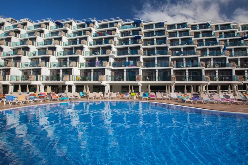 Bâtiment blanc à balcons donnant sur une piscine et des transats.