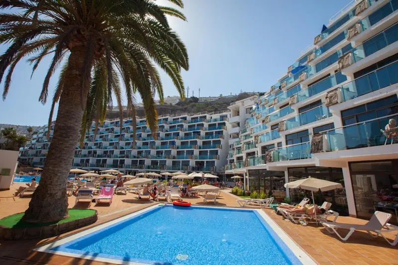 Bâtiment blanc moderne avec des balcons surplombant une piscine et une plage.