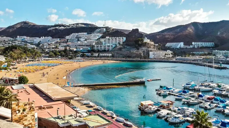 Vue aérienne d'une plage ensoleillée bordée de bâtiments et de montagnes.