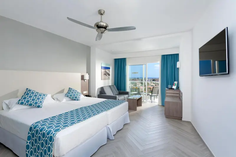 Une chambre lumineuse avec un grand lit et un canapé face à une baie vitrée.