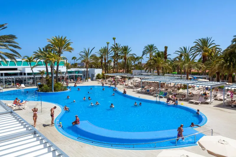 Une grande piscine rectangulaire bordée de transats sous des parasols.