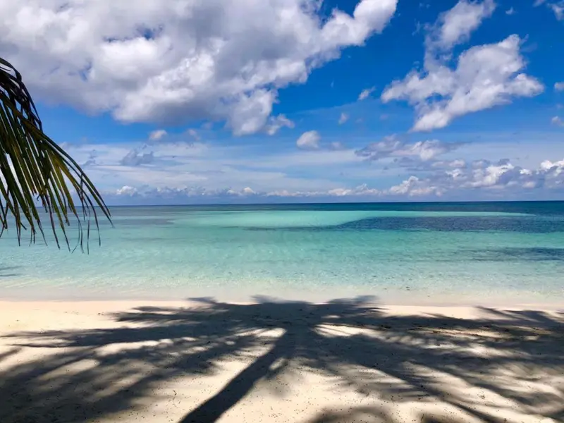 Plage de sable blanc bordée d'eau turquoise sous un ciel nuageux.