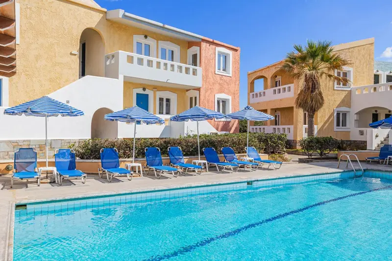 Transats bleus alignés au bord d'une piscine turquoise devant un bâtiment pastel.
