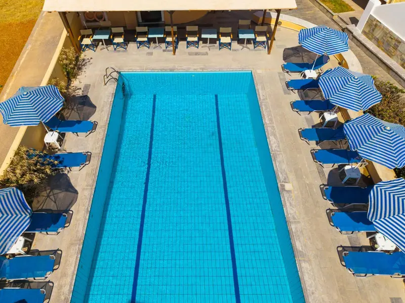 Vue aérienne d'une piscine rectangulaire entourée de transats et de parasols rayés.