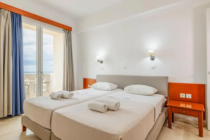 Chambre lumineuse avec deux lits simples et balcon.