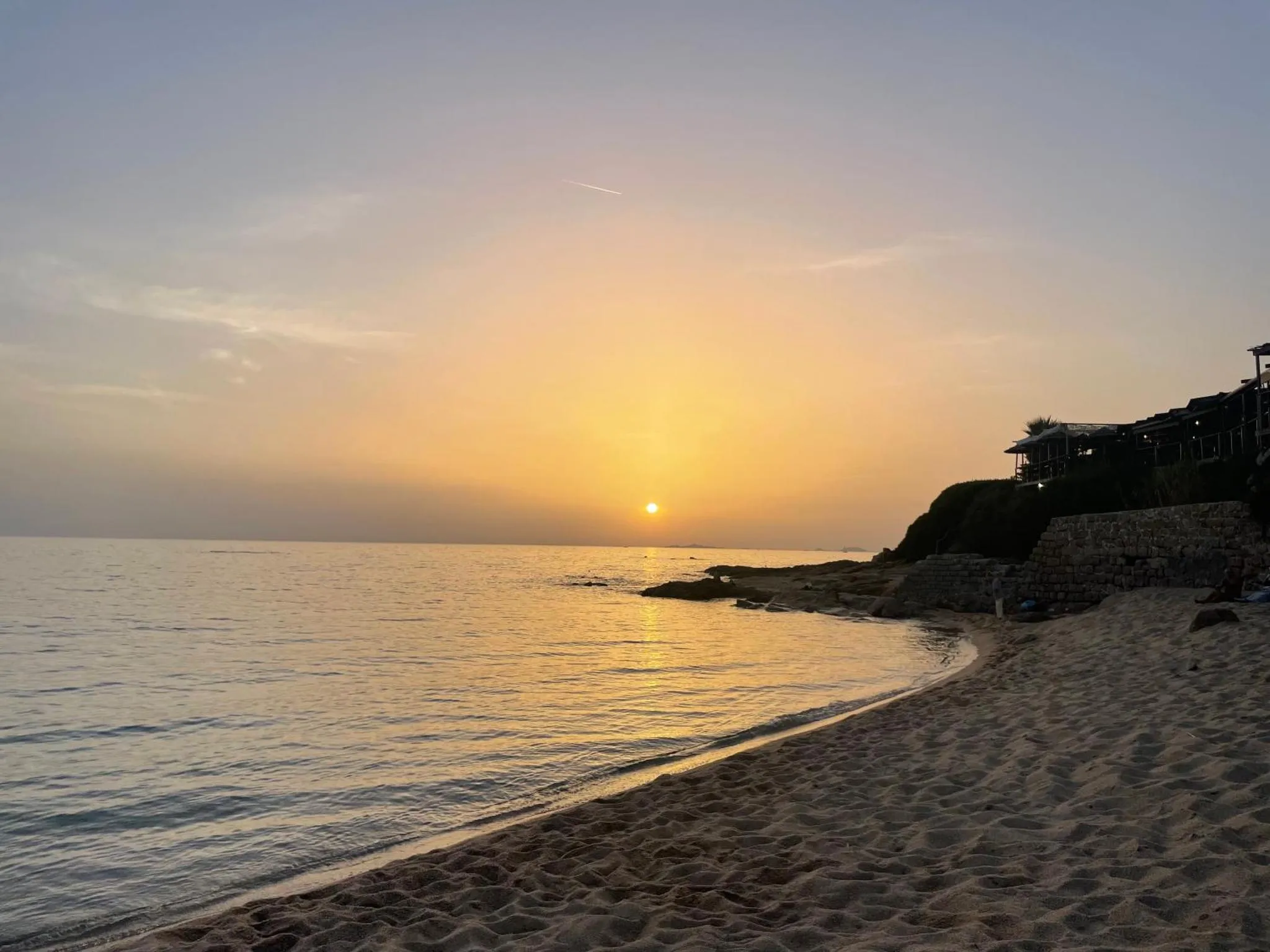Coucher de soleil sur une plage de sable fin avec une mer calme.