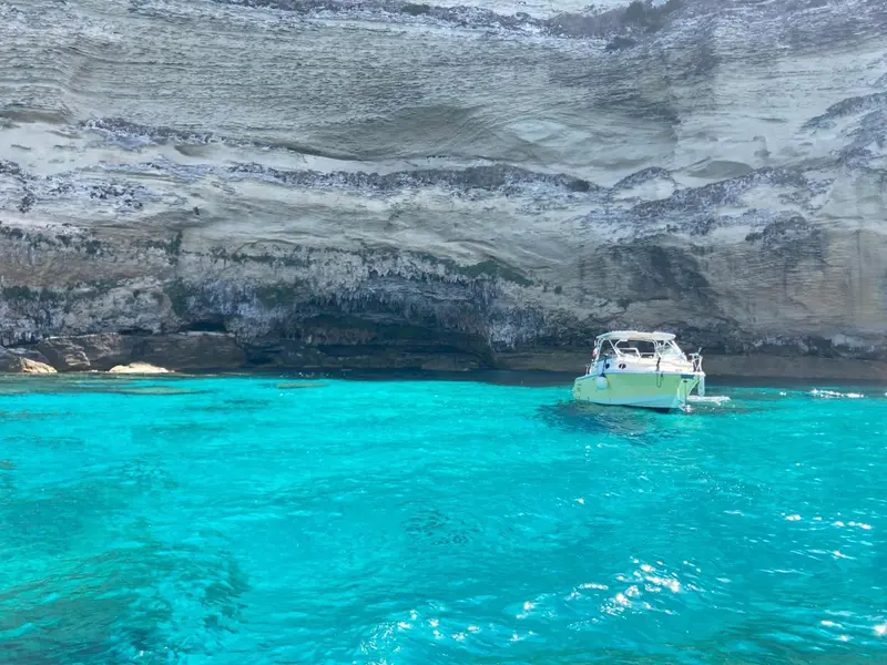 Un bateau de plaisance navigue dans une crique aux eaux turquoise.