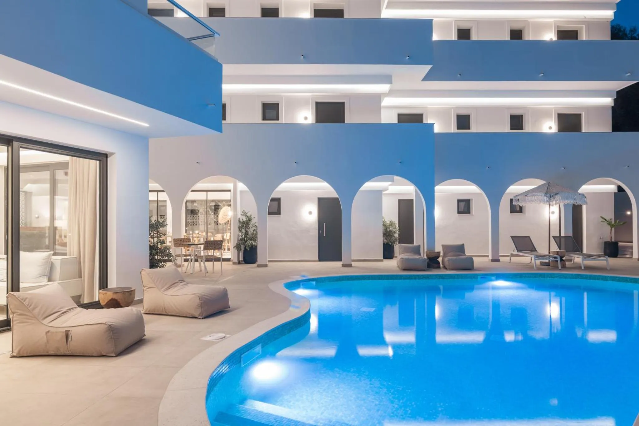 Une piscine illuminée s'intègre à un espace extérieur aménagé avec des fauteuils et des plantes.