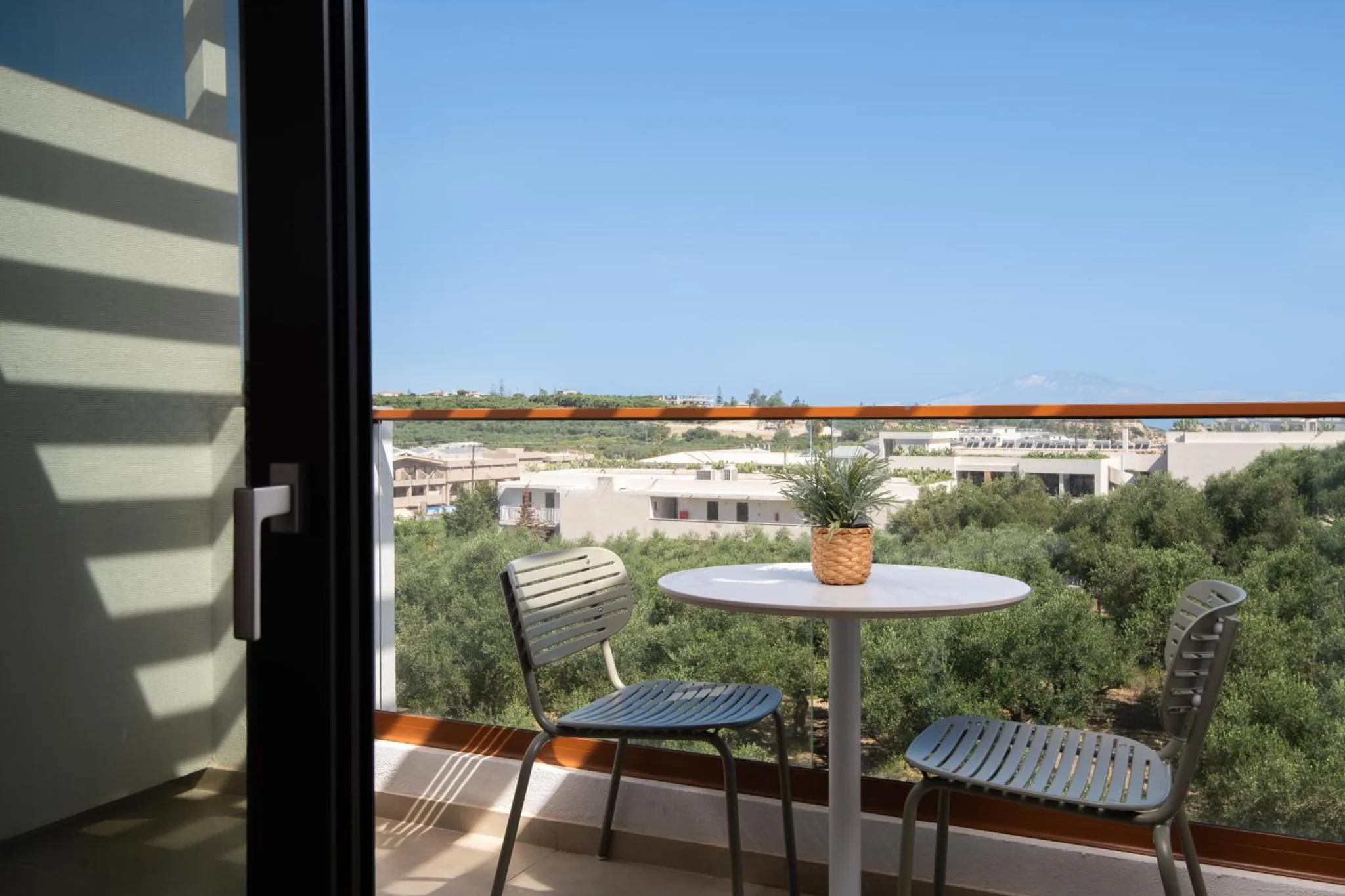 Une terrasse avec une table et des chaises offre une vue sur la mer et la végétation.