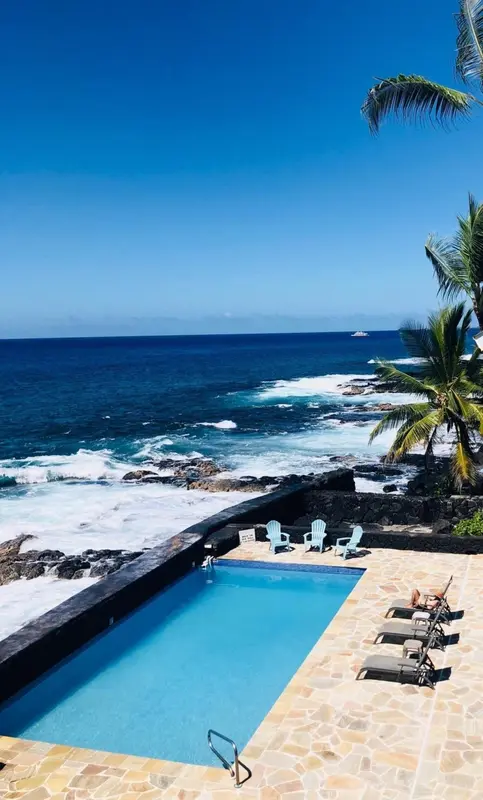Une piscine rectangulaire bordée de chaises longues surplombe la mer.
