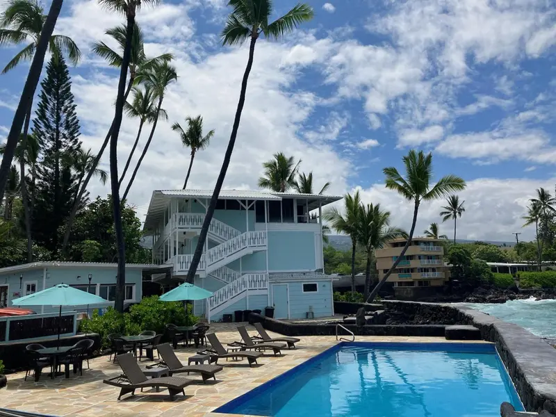Bâtiment bleu clair avec escalier extérieur surplombant une piscine et une plage.