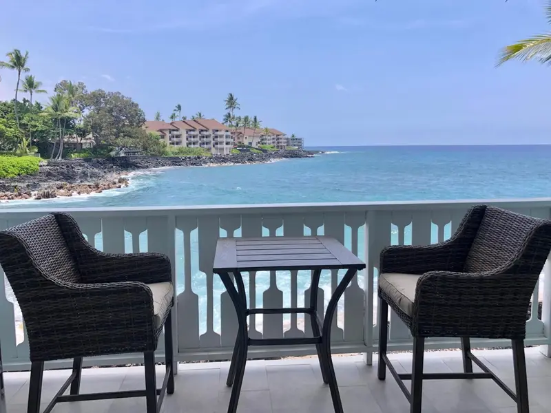 Deux fauteuils en osier et une petite table sur une terrasse avec vue sur la mer.
