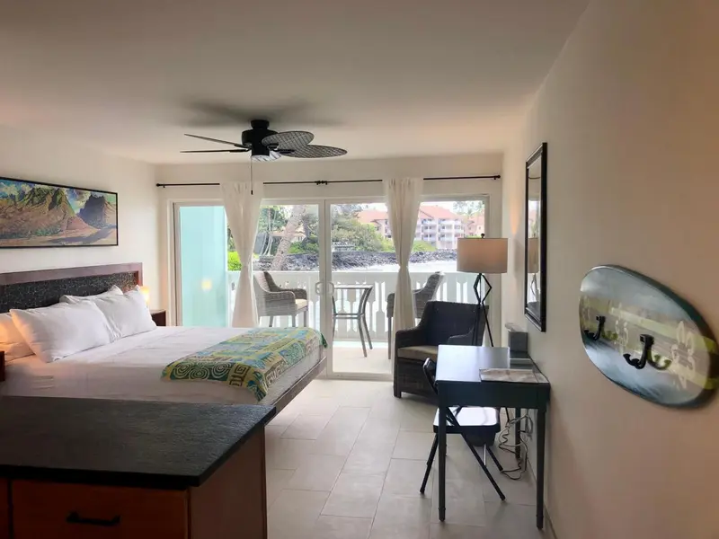 Chambre lumineuse avec un grand lit et un bureau près d'une baie vitrée donnant sur une terrasse.