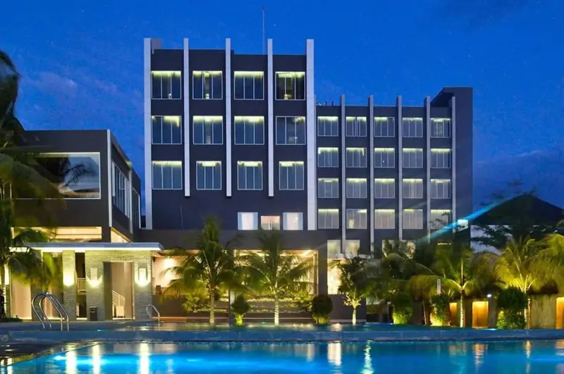 Bâtiment moderne illuminé la nuit avec une piscine au premier plan.
