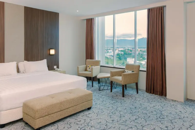 Une chambre lumineuse avec un grand lit et deux fauteuils près d'une fenêtre.