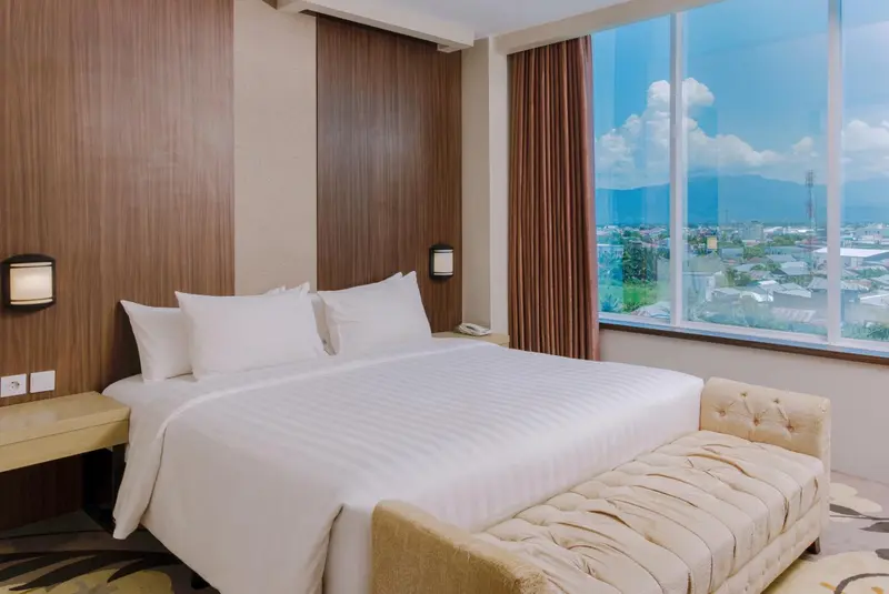 Chambre d'hôtel lumineuse avec un grand lit et une vue sur la ville.