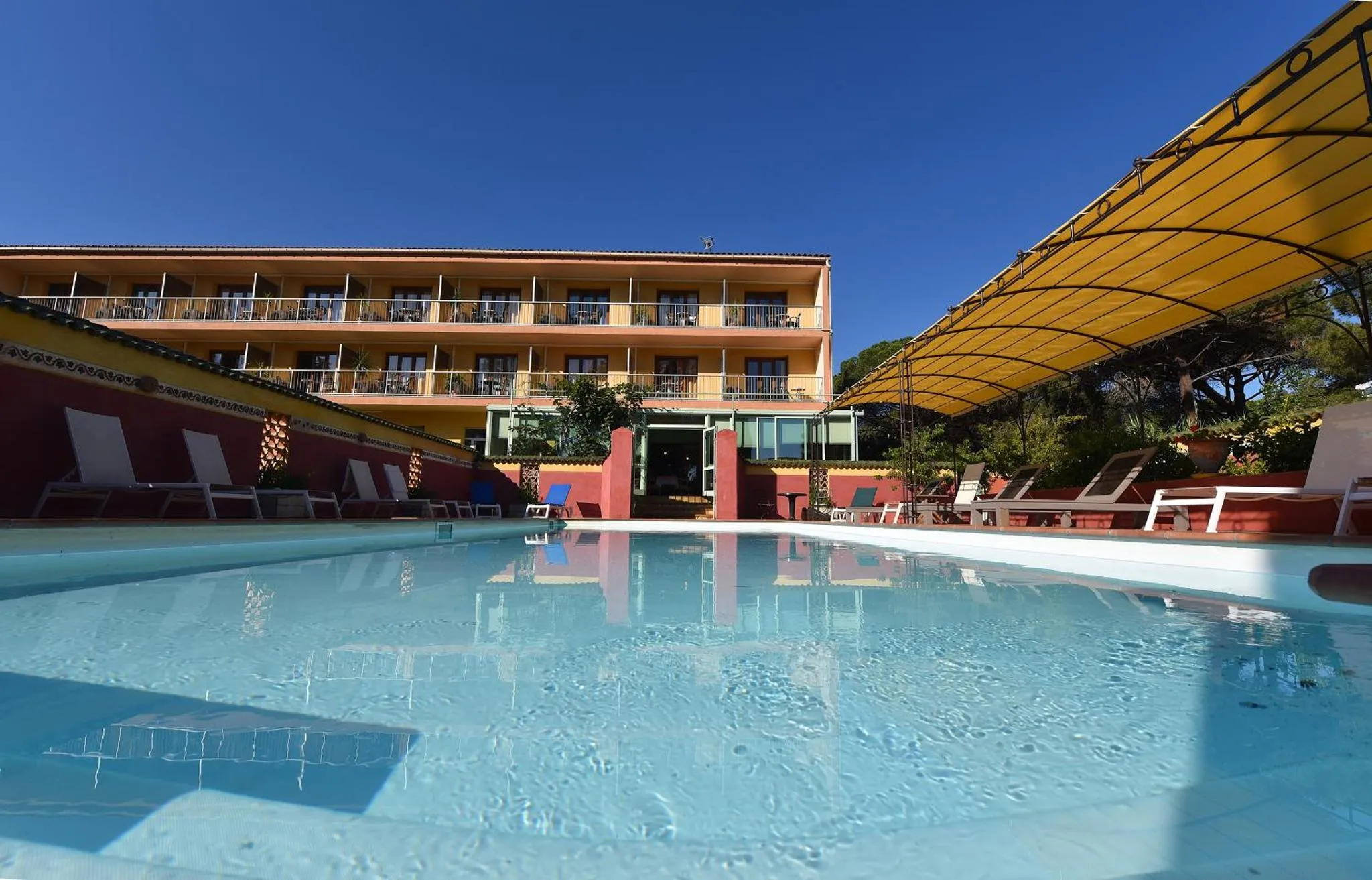 Piscine rectangulaire turquoise reflétant un bâtiment aux couleurs pastel sous un ciel bleu.