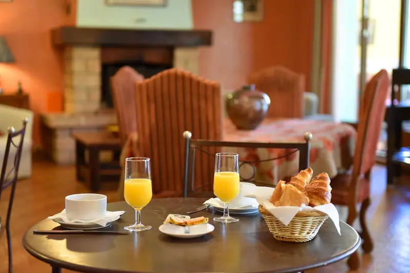 Une table est dressée avec des jus d'orange, une tasse de café et des viennoiseries.