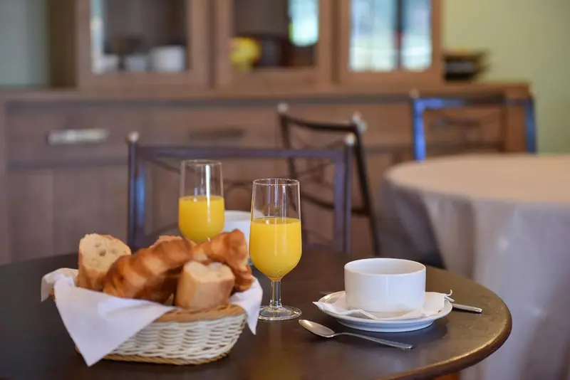 Une table ronde est dressée avec des viennoiseries, du jus d'orange et une tasse de café.