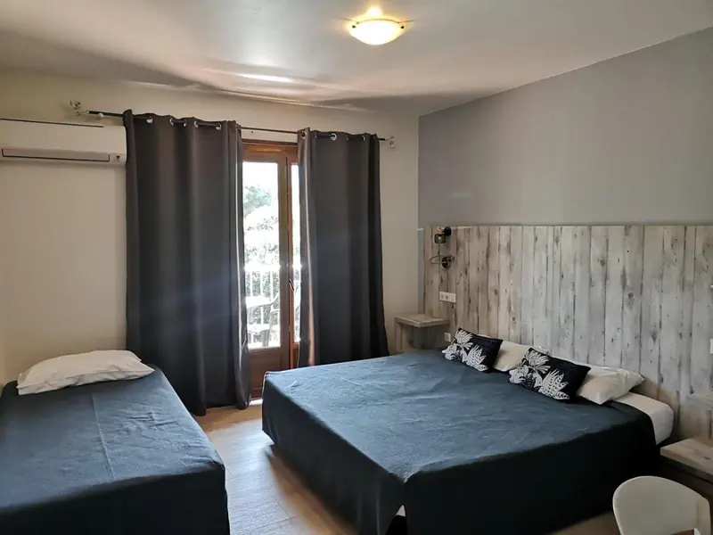 Une chambre avec deux lits et une porte-fenêtre donnant sur l'extérieur.