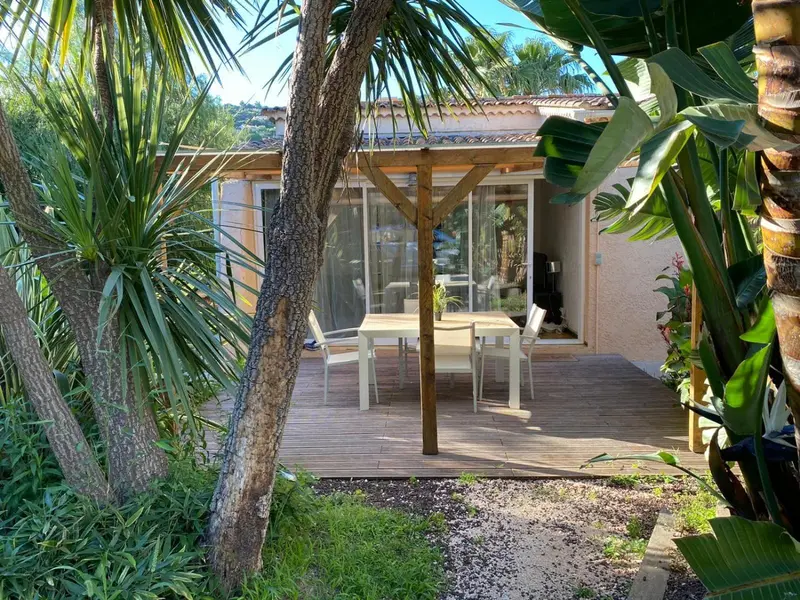 Terrasse en bois avec table et chaises devant une ouverture sur un espace intérieur.